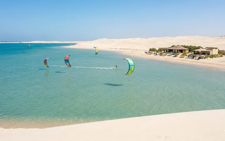 Turquoise lagoon of Dakhla lined with white dunes, with kitesurfers on the water